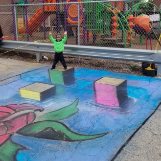 A child poses on one of Shaun Hays' 3D Chalk Art Creations in Humbolt Park during an after school celebration of the Arts.